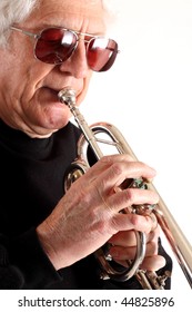 Old Man With Long White Hair And Dark Glasses Dressed In Black Playing A Silver Trumpet Against A White Background