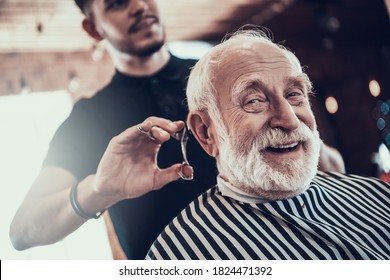 An old man looks at the camera while the master cuts his hair in a barbershop. An adult sidoy dede looks at the camera while he gets a stylish haircut. 