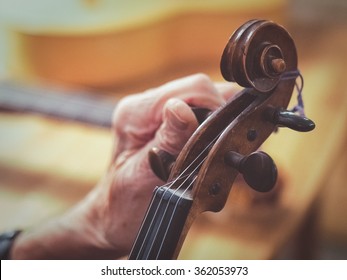 An old man (luthier) with aged hands is tuning a violin. You see other instruments like a guitar blurred in the background.
 - Powered by Shutterstock