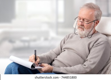 Old Man Making A Shopping List With A Pen On Paper For Holidays