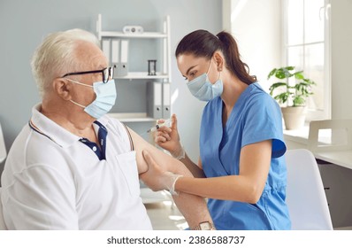 Old man in medical face mask getting injection Covid-19 vaccine at hospital during immunization campaign. Doctor or nurse holding syringe and giving shot to his shoulder. Global pandemic, vaccination. - Powered by Shutterstock