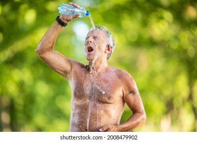 Old Man With No Shirt Pours Water From A Bottle Over His Head And Face Outdoors On A Hot Summer Day.