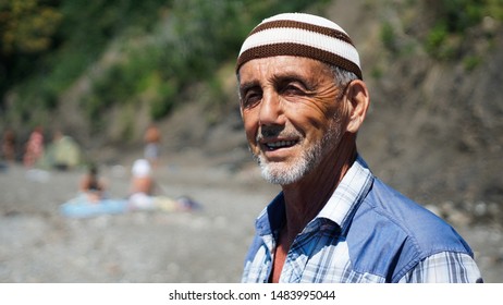 Old Man On The Beach. Cheerful Sunburnt Man Smiling And Squinting Enjoying Long Warm Vacation.