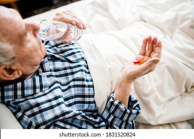 Old Man In Pajamas Drinking Glass Of Water And Have Pills In His Hand While Laying At The Bed. Stock Photo