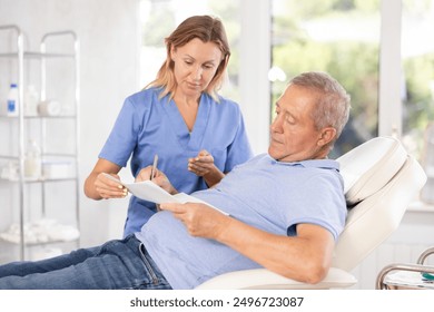 Old man patient signing documents together with female physician in light doctor's cabinet - Powered by Shutterstock