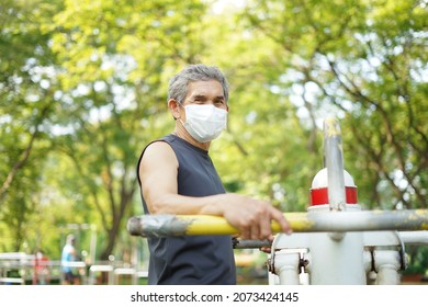 An Old Man With Protective Face Mask Doing Exercise At Outdoor Fitness Equipment In The Park(selective Focus), Concept Elderly People Exercise In Public Area, Lifestyle