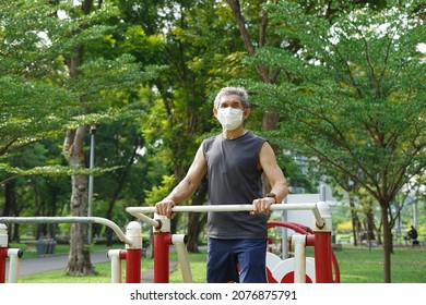 An Old Man With Protective Face Mask Doing Exercise At Outdoor Fitness Equipment In The Park(selective Focus), Concept Elderly People Exercise In Public Area, Lifestyle, Safety From Covid-19 