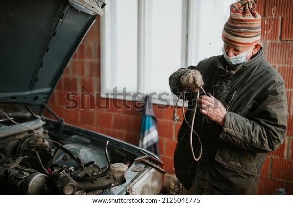 Old man with protective mask in the garage repair\
his old car.