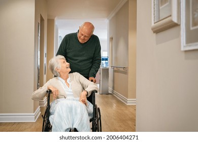 Old man pushing disabled wife on wheelchair in hospital hallway. Happy smiling senior woman in a wheelchair relaxing with her husband in care centre during a visit. Elderly man pushing his old wife. - Powered by Shutterstock