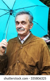 Old Man In The Rain With Umbrella Looking At The Camera 