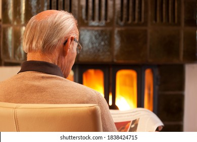 Old Man Reading Newspaper While Sitting By A Fireplace In A Living Room - Selective Focus On The Head