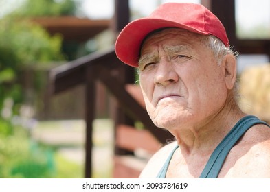 An Old Man In A Red Baseball Cap, Basking In The Sun In Summer