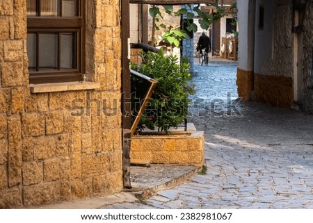 Old man riding a bicycle, in the 
alley street of Ohrid City. Sunrise. Morning sun. Brown wooden window frame, part of the building architecture. Macedonia 2023.