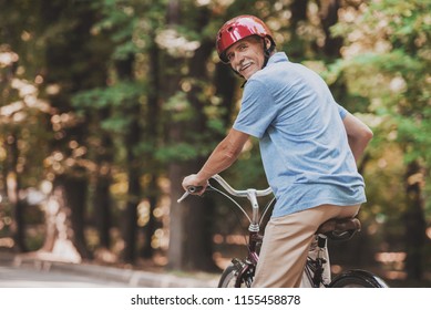 Old Man Riding On Bicycle In Park In Summer. Healthcare Concept. Relaxing In Park. Active Rest Concept. Riding On Bicycle. Smiling Grandfather. Man With Gray Hair. Healthy Lyfestyle In Summer.