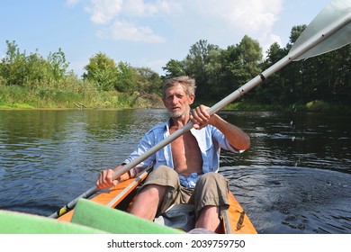 An Old Man Rowing A Kayak While Traveling Along The River.