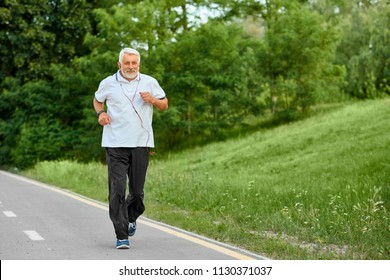 Old man running on modern city park's racetrack. Exercising alone in summer, spring. Outdoors sport, trainings. Wearing classic white shirt with dark blue stripes,black trousers, sneakers.