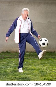 Old Man In Seventies Kicking A Soccer Ball In Courtyard