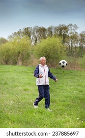 Old Man In Seventies Kicking A Soccer Ball In Park