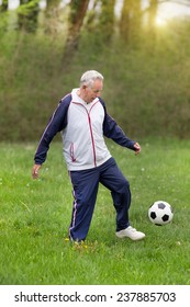 Old Man In Seventies Kicking A Soccer Ball In Park