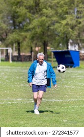 Old Man In Seventies Kicking A Soccer Ball On The Field