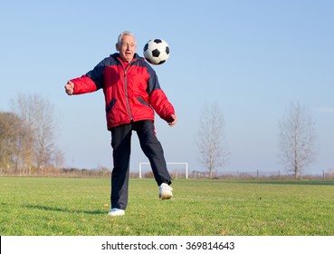 Old Man In Seventies Kicking A Soccer Ball On Playground