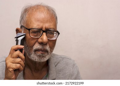 An Old Man Shaving His Beard With An Electric Razor. Concept Of Technology For Everyone. Selective Focus.