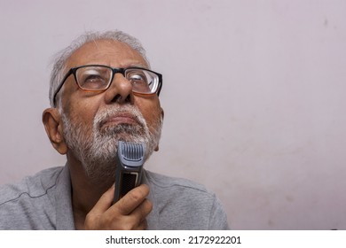 An Old Man Shaving His Beard With An Electric Razor. Concept Of Technology For Everyone. Selective Focus.