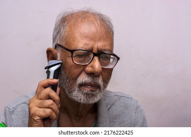 An Old Man Shaving His Beard With An Electric Razor. Concept Of Technology For Everyone. Selective Focus.