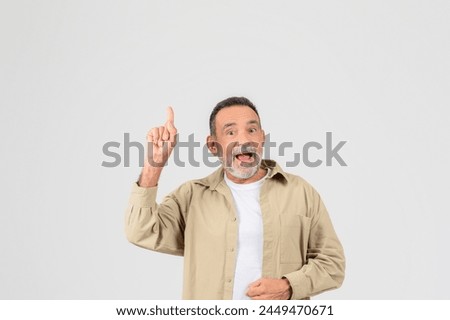 An old man shows excitement, pointing up enthusiastically, isolated on a neutral background, copy space
