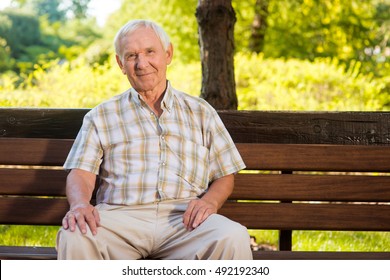 Old Man Sits On Bench. Elderly Guy Is Smiling. He Deserves A Good Rest. All Problems Left Behind.