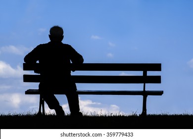 old man sitting alone on park bench under tree