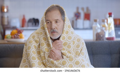 The Old Man, Sitting In His Cold House With A Blanket Wrapped, Trembles With Cold And Tries To Keep Warm. Close Up. Heating Problem, Cold House Concept. 