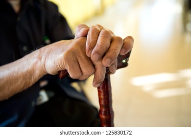 Old Man Sitting With His Hands On A Wooden Walking Stick.