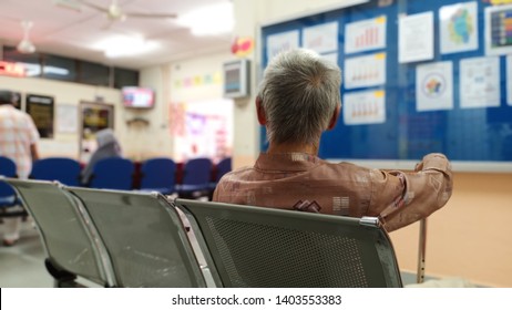 old man sitting on bench waiting for his number called  in the hospital . holding a cane and watching tv -image