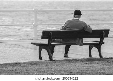 Old man sitting on a bench facing the sea
