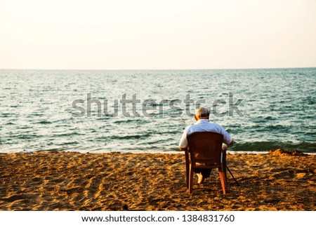 old man sitting on a chair on the beach and looking at the sea.