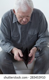 Old Man Sitting On A Couch And Looking At An Empty Wallet