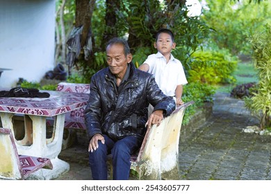 An old man sitting at a stone table With a grandchild giving a back massage - Powered by Shutterstock