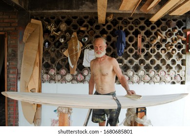 An old man skillfully repairs a balsa-crafted surfboard in a workshop, showcasing his craftsmanship and dedication to the art of surfing. - Powered by Shutterstock