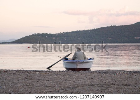 Old man in a small boat getting ready for fishing at seaside of Turkbuku village in Bodrum peninsula. Sea and landscape are in the view. Conceptual image showing the Aegean culture and lifestyle.