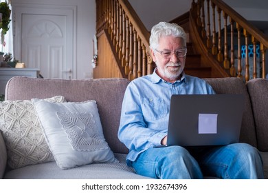 Old Man Smiling Sitting On The Sofa In The Living Room Using Laptop, Enjoying Working With Computer Feeling Satisfied Sending Messages, Calling Friends, Surfing Web Online Concept