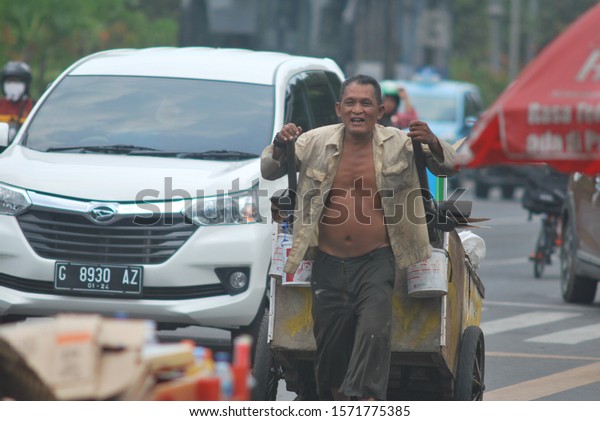old man smiling while\
dragging hes one and only home and shelter in this world. he is a\
pemulung or scavenger in jakarta, Indonesia. photo taken in 9\
November 2019