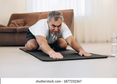 Old Man In Sportswear Lying On Mats Doing Child Asana, Exercise Calms Body And Mind, Stretching Hands Forward. Practicing Yoga At Home. Wellness Concept. Man Training To Have Flexible Body.