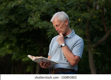 Old Man Standing And Reading Book In Park. Outdoor