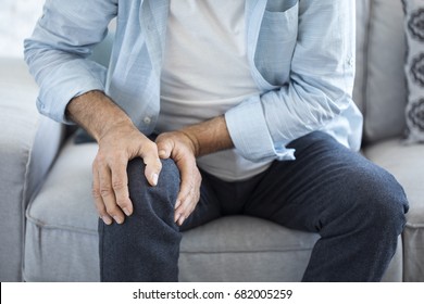 Old man suffering from knee pain sitting sofa