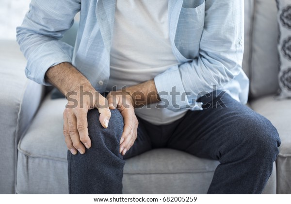 Old man\
suffering from knee pain sitting\
sofa