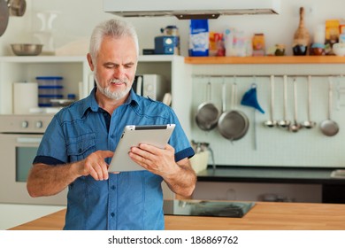 Old Man With Tablet Sitting At The Kitchen