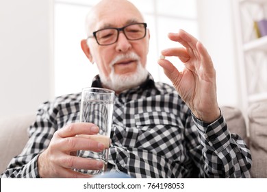 Old man taking pills with water glass. Healthcare, treatment, aging concept - Powered by Shutterstock