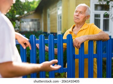 Old man talking with his neighbour beside fence of country house.