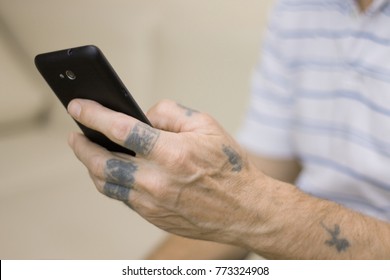 Old man with tattooed hands using a black smartphone, close-up